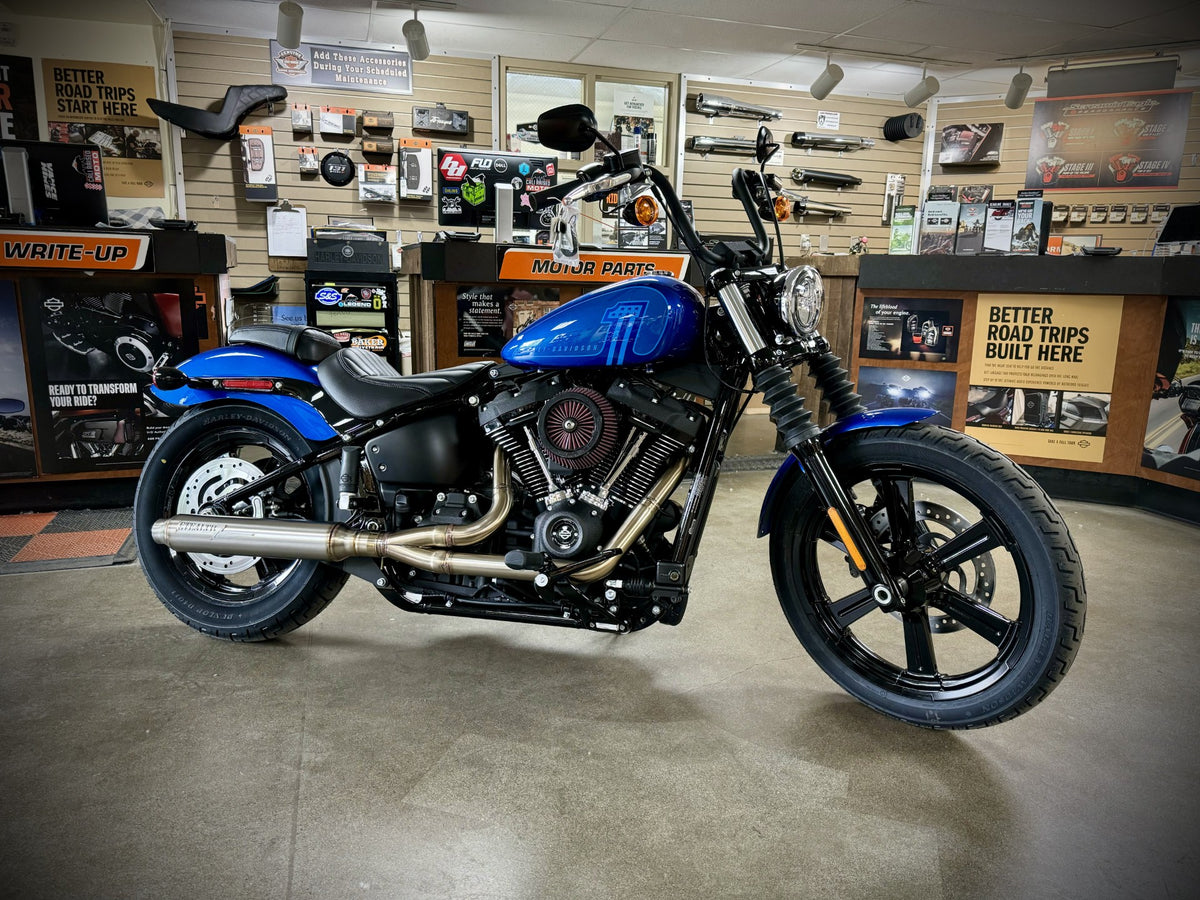 A black motorcycle with the focus on the exhaust system, which is silver in color. The motorcycle is parked against a plain wall backdrop., photo 33 of 36